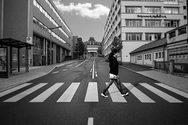 A black-and-white photo of a person crossing a road at a crosswalk
